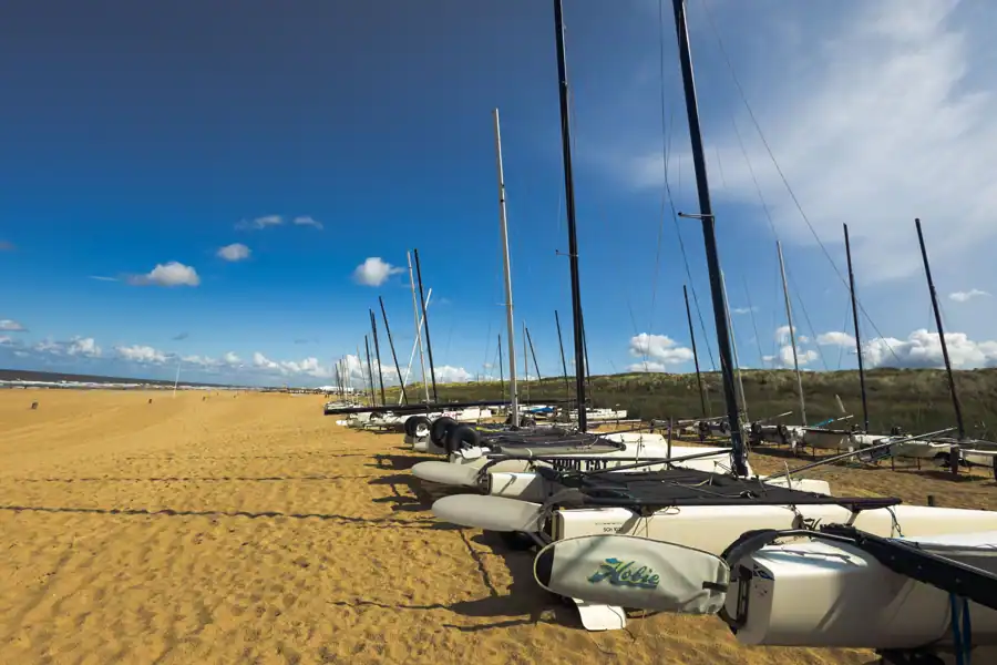 Sailboats lined up on Den Haag beach, sunny summer day with clear blue sky.