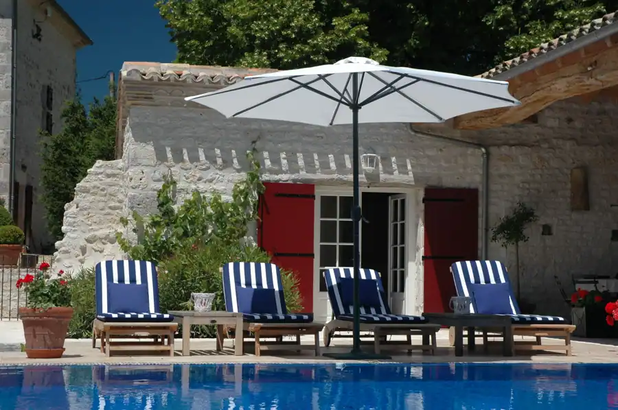 Relax by a stone house pool with loungers and umbrellas in a sunny yard.