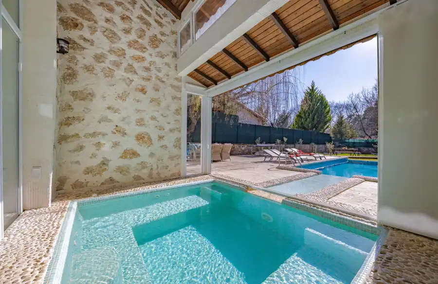 Modern villa featuring indoor and outdoor pools with elegant loungers.
